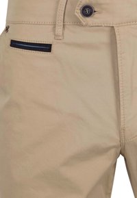 Beige broek met een gladde textuur, voorzien van een zichtbare knop, een schuin zakje en subtiele stiksels.