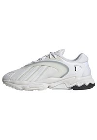 Athletisk sneaker i vitt med mesh-ovandel, texturerade accenter, grå detaljer, vadderad sula och svart yttersula, med böjda designlinjer.