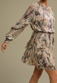 Kwiatowa sukienka z długimi rękawami, z falbaniastymi akcentami, w delikatnych pastelowych kolorach. Wykonana z teksturowanej tkaniny, z dopasowanym stanem i zwiewną spódnicą.