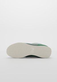 Green sneaker with a textured fabric upper, a white rubber sole featuring a herringbone pattern, and a visible logo on the side.