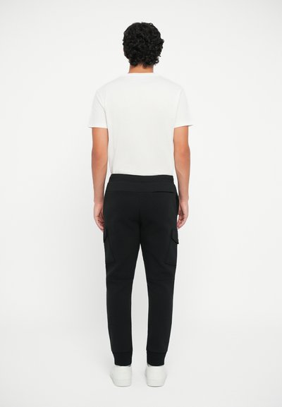 Pantalonii cargo negri au buzunare laterale, un design cu picior tapered și un brâu elastic, asortați cu un tricou simplu alb cu mânecă scurtă.