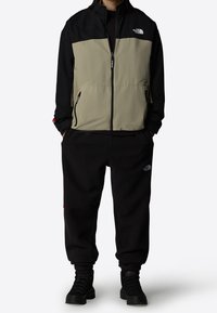 Sort og olivengrøn jakke med lynlåslukning og lommer, kombineret med sorte fleecebukser med logo og tekstureret stof.