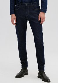 Dark blue denim jeans with a straight fit, featuring front pockets, a zip fly, and subtle stitching details. Worn with black ankle boots.