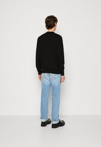 Schwarzes Langarmoberteil, hellblaue Jeans und schwarze Schuhe. Das Oberteil hat einen Rundhalsausschnitt; die Jeans haben einen geraden Schnitt und leichte Abnutzungen.