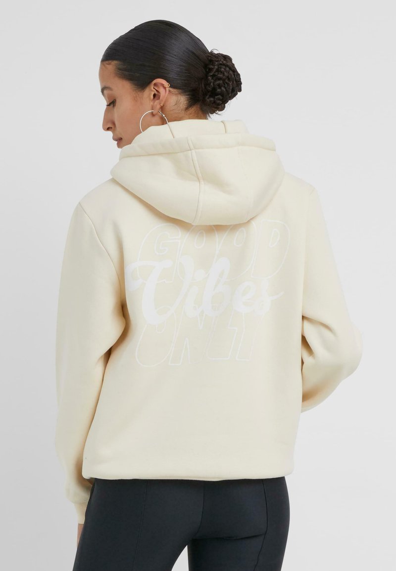 Cremfarbener Hoodie mit einem großen weißen Aufdruck "GOOD VIBES ONLY" auf dem Rücken. Mit Kapuze mit Zugband und gerippten Bündchen.