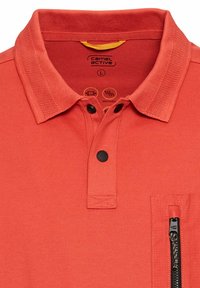 Rode polo shirt gemaakt van ademend materiaal, met een gestructureerde kraag, twee zwarte knoopsluitingen en een zijvak met ritssluiting.