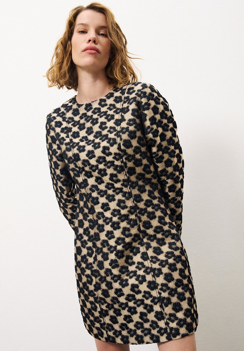 Tijgerprint jurk met een beige basis en zwarte vlekken, lange mouwen, ronde halslijn en getailleerde silhoutte. Textuurstof met naaddetails.