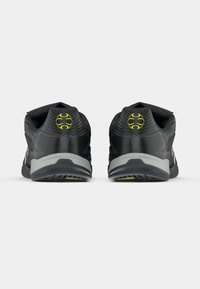 Μαύρα αθλητικά παπούτσια με αεροδυναμικό σχέδιο, με υφή στην επάνω επιφάνεια, αντανακλαστικές λεπτομέρειες και λογότυπο σε νέον κίτρινο στο τακούνι.