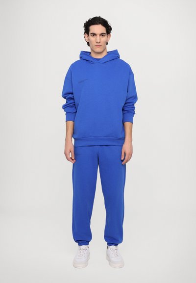 Sweatshirt bleu et joggeurs assortis en tissu doux. Le hoodie est doté d'une poche kangourou et d'un petit logo noir sur le devant.