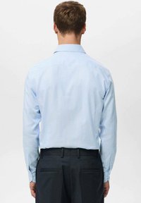 Svijetloplava prugasta košulja s rasprostrtim ovratnikom, dugim rukavima i manžetnama na gumbe. Nošena s tamnim hlačama, vidljiv stražnji pogled.