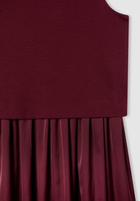 Bordowa sukienka z dopasowaną górą wykonaną z gładkiego materiału oraz plisowanym, satynowym dołem. Bezszwowy fason o miękkiej teksturze.