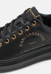 Crne kožne tenisice sa zlatnim okicama i utisnutim logotipom. Sadrže crne vezice i teksturiranu gumenu đonu.