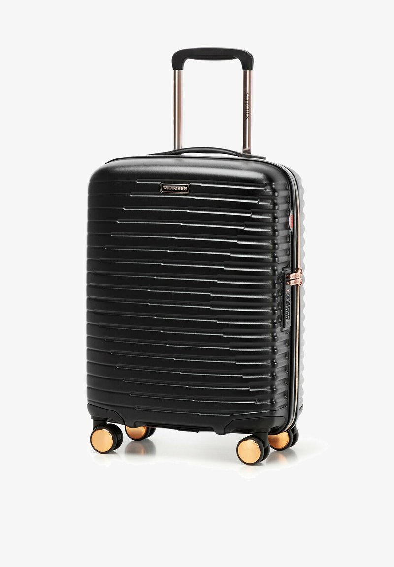 Czarna walizka twarda z żłobionym wzorem, różowo-złotymi akcentami, teleskopową rączką i czterema kółkami zapewniającymi manewrowość. Widoczne logo marki.