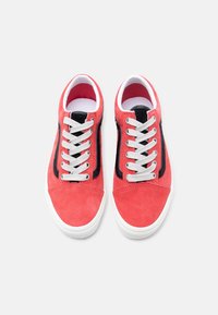 Ζευγάρι κόκκινα σαμουά παπούτσια με άσπρες σόλες και κορδόνια, με μια μαύρη ρίγα στα πλαϊνά, σε θέα από πάνω σε λευκό φόντο.