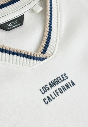 Sweatshirt blanc avec un col côtelé bleu marine et beige. Porte l'inscription brodée "LOS ANGELES CALIFORNIA" en bleu foncé sur le devant.