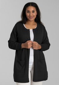 Schwarze Strickjacke aus weichem Material mit rundem Ausschnitt, langen Ärmeln, offener Vorderseite und zwei vorderen Taschen.