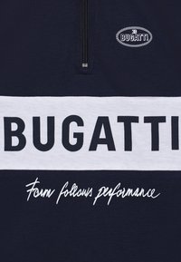 Pullover blu navy con zip, caratterizzato da una banda orizzontale bianca con "BUGATTI" in bold nero e la frase "La forma segue le prestazioni" in corsivo bianco.