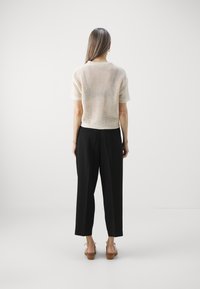 Kurzärmliges, cremefarbenes Stricktop mit Polo-Kragen, kombiniert mit schwarzen, lässig geschnittenen Hose und braunen, Blockabsatzsandalen.