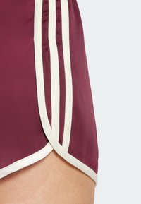 Pantalones cortos deportivos burdeos con franjas blancas en los laterales, textura suave y detalle de dobladillo doblado para un diseño de ropa activa.
