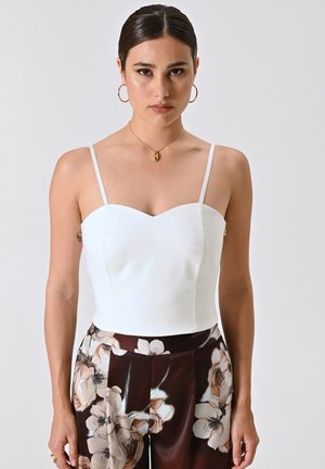 White, fitted bustier top with thin straps and a sweetheart neckline, paired with patterned brown floral trousers. Smooth texture, minimal design.