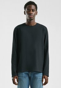 Zwarte lange mouw t-shirt met een ronde halslijn en een relaxed fit, gemaakt van zachte katoen. Gecombineerd met lichtblauwe denim jeans.