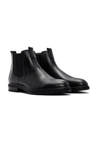 Botas Chelsea negras de cuero con textura suave, paneles laterales elásticos, diseño minimalista y suela de goma de perfil bajo.
