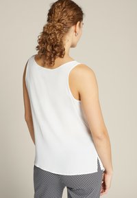 Witte mouwloze top met een ronde halslijn, een gladde textuur en zijsplitten, gecombineerd met een zwart-wit gestreepte broek.