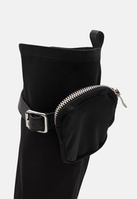Sorte støvler med en elegant, glat overflade. Har en sølv lynlås lomme, et justerbart sort bælte og et rundt topdesign.
