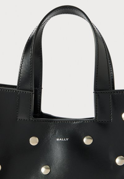 Sac à main en cuir noir avec des clous en ton or et un logo. Texture lisse avec double poignées et un design structuré.