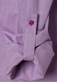 Manche d’une chemise violette retroussée et maintenue par une sangle fermée par un bouton violet assorti.