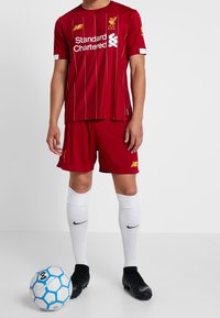 Röd Liverpool FC-fotbollströja med randigt mönster, försedda med en logotyp, och matchande shorts. Vita strumpor och svarta fotbollsskor, med en svart och blå fotboll.
