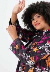 Chaqueta negra con gráficos multicolores llamativos, incluyendo estrellas y patrones de animales. Tiene mangas anchas y un corte relajado.