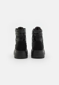 Botas negras hasta el tobillo con un diseño acolchado y acolchado. Presenta acentos de ante negro y una suela de goma texturizada. Incluye lengüetas en la parte posterior.