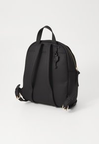 Sac à dos noir en matériau lisse, doté de bretelles doublées, d'une poignée en haut et d'une fermeture éclair dorée avec un détail clé.