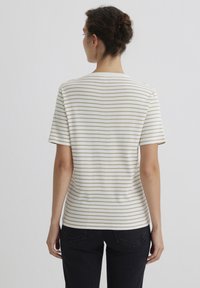 Weiß gestreiftes T-Shirt mit dünnen beigen horizontalen Streifen, kurzen Ärmeln und rundem Ausschnitt, kombiniert mit dunklen Jeans.