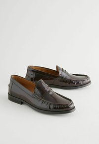 Mocasines de cuero marrón oscuro con un acabado suave, que presentan una banda decorativa de costura y un tacón bajo en bloque. Forma clásica y estilizada.