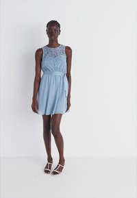 Svijetloplava haljina s čipkastim gornjim dijelom, bez rukava, i lepršavom suknjom s podesivim pojasom i bočnim džepovima.