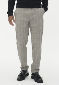 Szare spodnie w kratę z żółtymi i niebieskimi liniami; dopasowany krój; tkanina teksturowana; połączone z czarnymi skórzanymi butami z frędzlami.