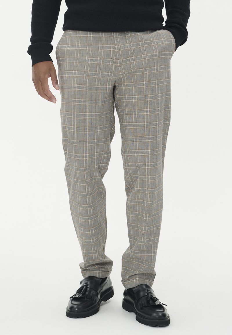 Szare spodnie w kratę z żółtymi i niebieskimi liniami; dopasowany krój; tkanina teksturowana; połączone z czarnymi skórzanymi butami z frędzlami.