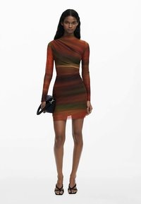 Långärmad, kroppsnära minimodell med gradient ränder i varma färger. Tillverkad av lätt, transparent tyg med en knutdetalj i sidan.