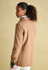 Brown checked blazer with a tailored fit, featuring a notched collar, buttoned cuffs, and a smooth texture. Accented with green sleeves.