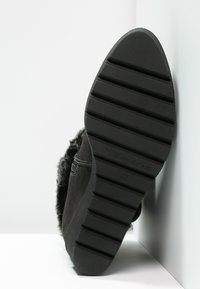 Černé semišové kotníkové boty s texturovanou gumovou podrážkou, která má horizontální drážky a značku "Tamaris" vyraženou na boku.