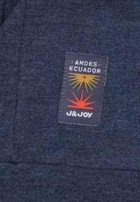 Marineblauwe stof met een stikselpatroon. Een rechthoekig label toont "ANDES ECUADOR" en "J&JOY," met gele en rode grafische accenten.