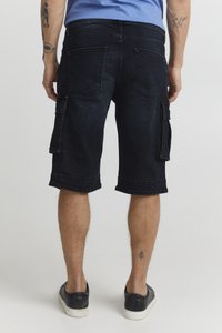 Tamno plave cargo kratke hlače do koljena, s bočnim džepovima, prevrnutim rubovima i čvrstom denim teksturom. Nosi ih s crnim cipelama.