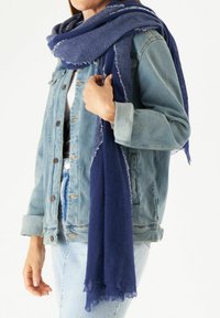 Écharpe bleu marine en tissu doux, avec un design texturé et des bords frangés, portée sur une veste en denim clair.