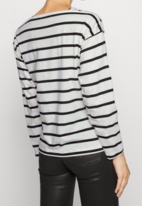Striped long-sleeve shirt in gray and black, featuring a boat neckline and a relaxed fit. Smooth fabric with horizontal stripes.