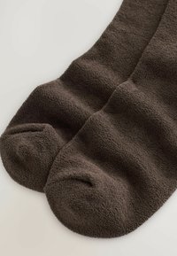 Hnedé, plyšové, textúrované ponožky s zaoblenými prstami, ktoré majú jemný povrch a ryhované časti pre zvýšenú flexibilitu.