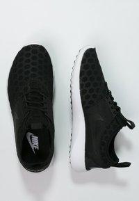 Svarta sportskor med ovandel i bikakestruktur, solid svarta detaljer, vita sulor och runda snören. Nike-logotyp på sidan och i innersulan.