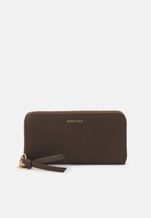 Portofel din piele ecologică maro, cu un logo auriu, închidere cu fermoar și un accent cu ciucure. Textură netedă, cu o formă rectangulară.