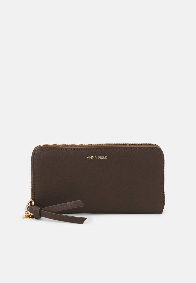 Carteira de imitação de couro castanha com um logótipo dourado, fecho de zip e um detalhe de franja. Textura suave com forma retangular.